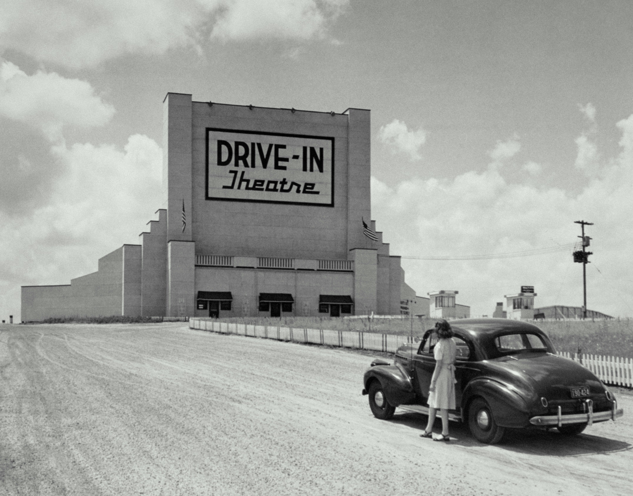 An old drive in movie theater with a woman outside a car