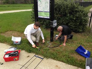 This is an image of 2 men installing equipment near a trailhead