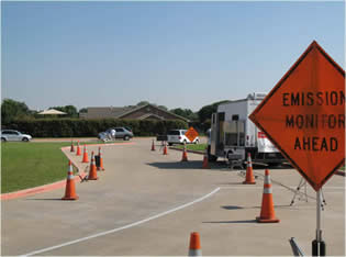 This is an image of a road with cones and a caution sign with the text "Emission monitor ahead"