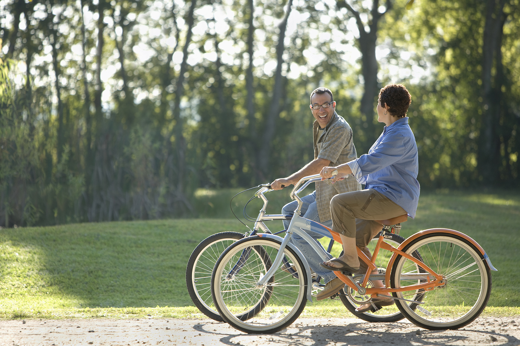 This is an image of a smiling couple riding bikes through a park
